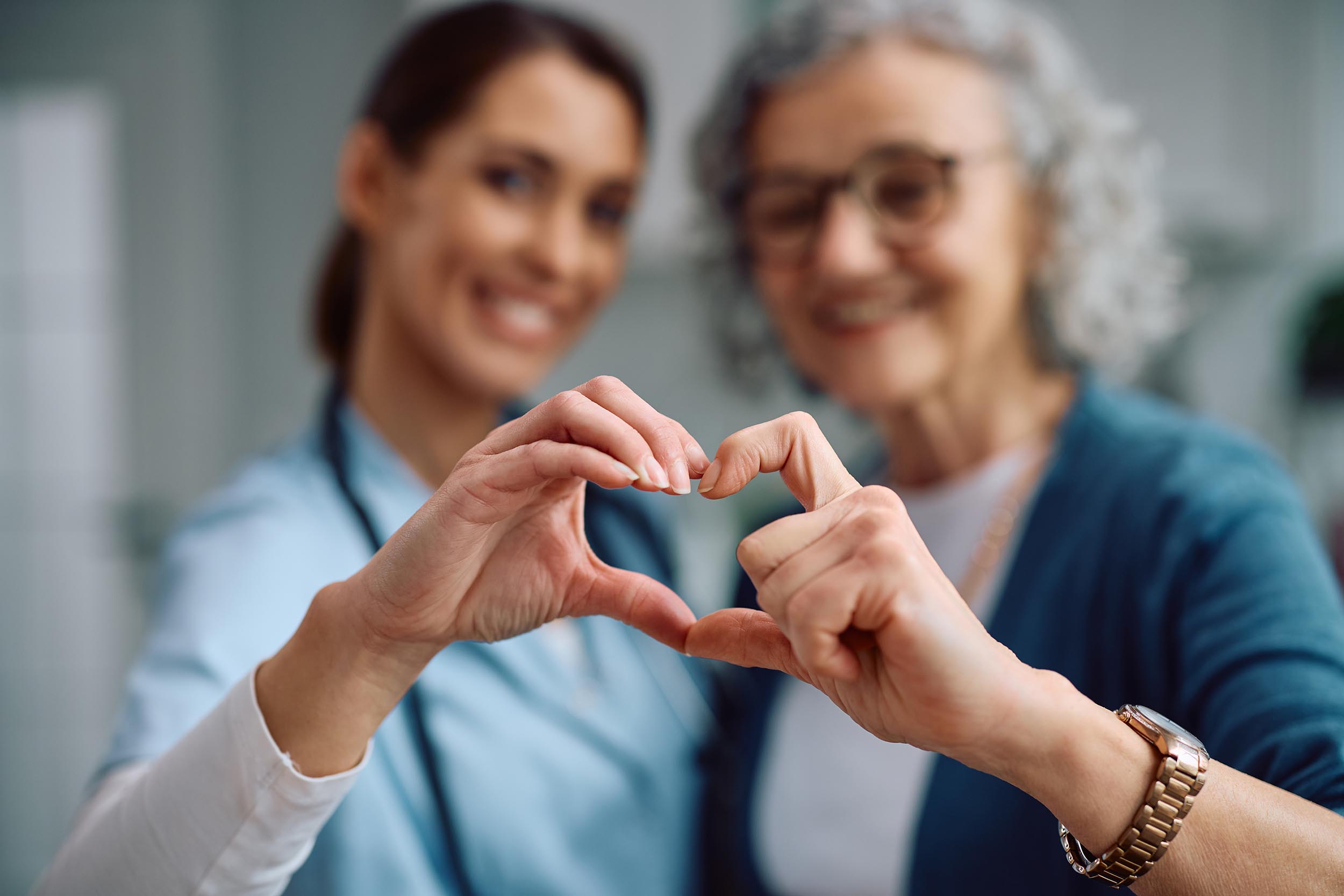 Close up of nurse and senior woman making heart shape with hands during home visit.